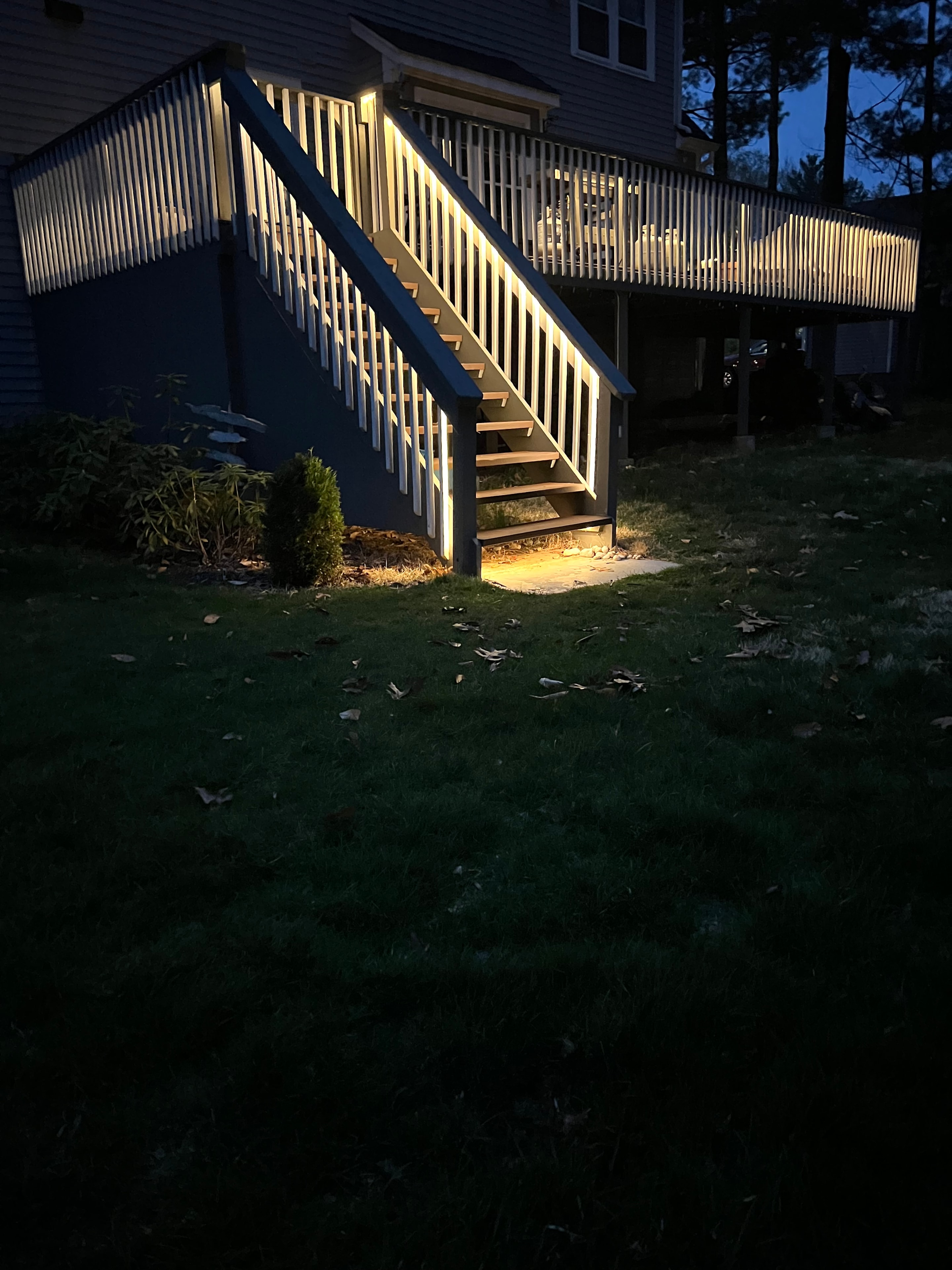 Under-rail LED strip lighting on a residential deck staircase to illuminate automatically at dusk.