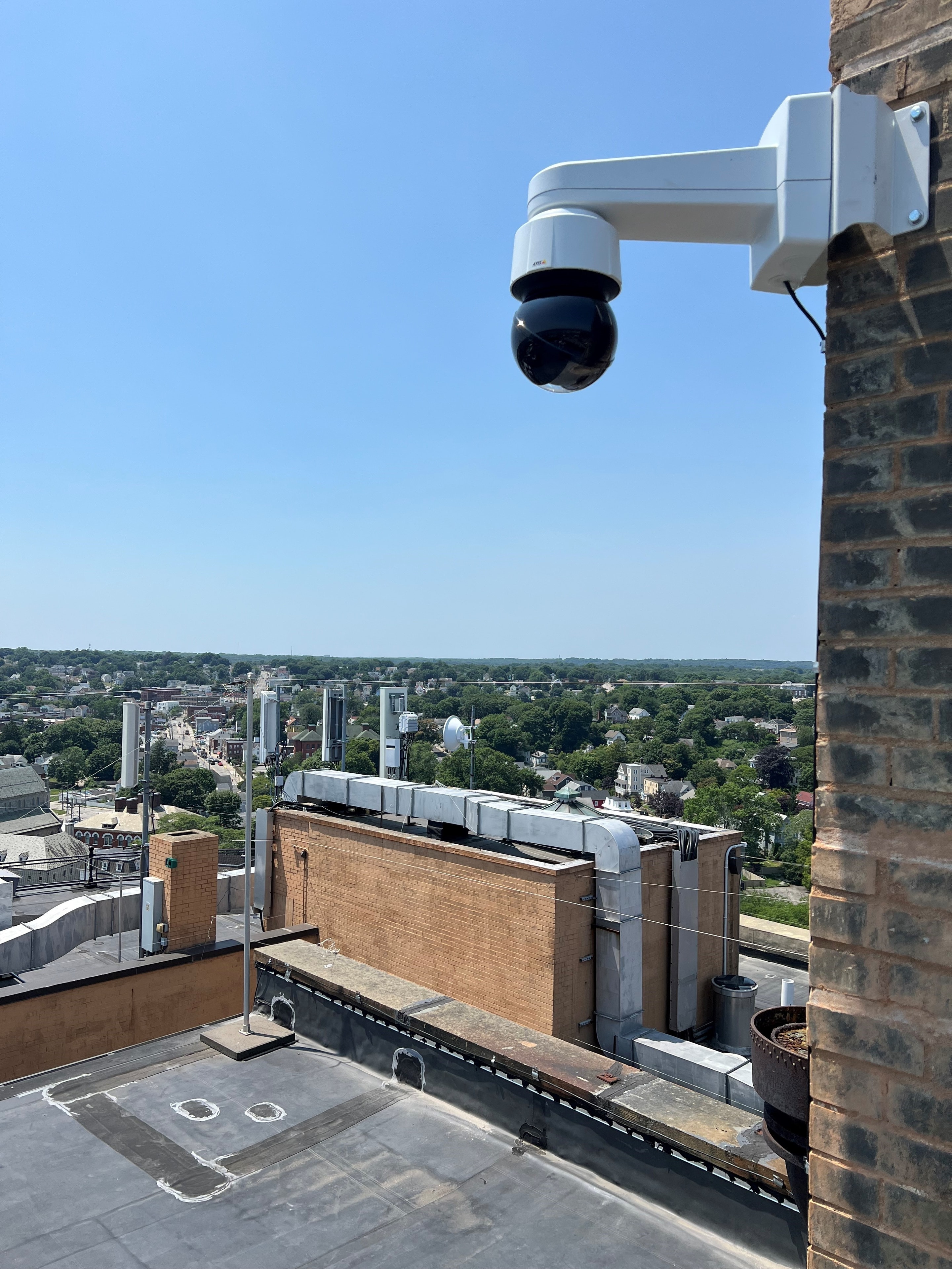 Axis PTZ security camera mounted on rooftop brick wall with panoramic city view